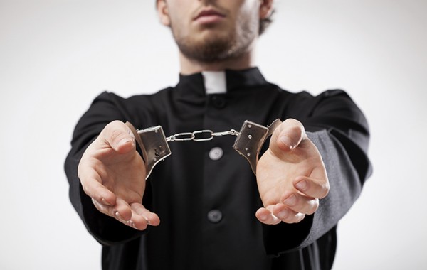 Young christian priest in cassock arrested and handcuffed
